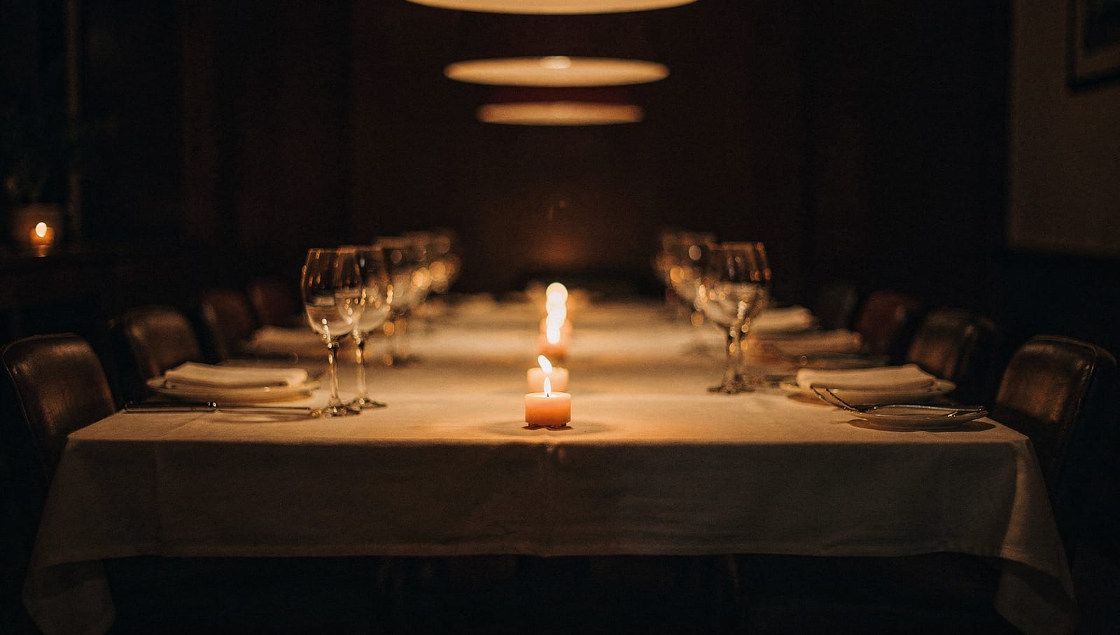 Long candlelit table set with white linen and wine glasses for a private dinner