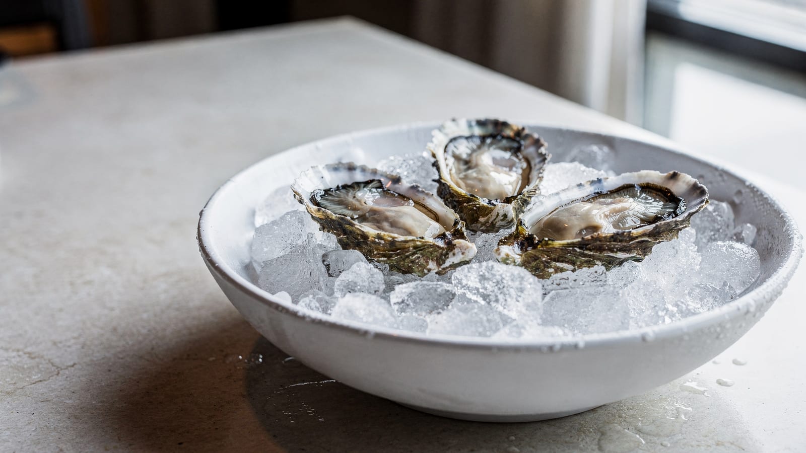 Three fresh oysters on the half shell over crushed ice in a white ceramic bowl