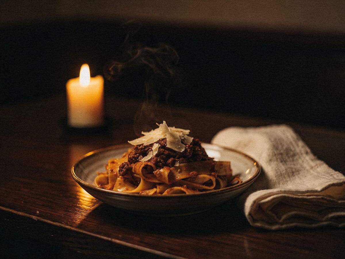 Bowl of handmade pasta with slow-cooked ragu in warm candlelight